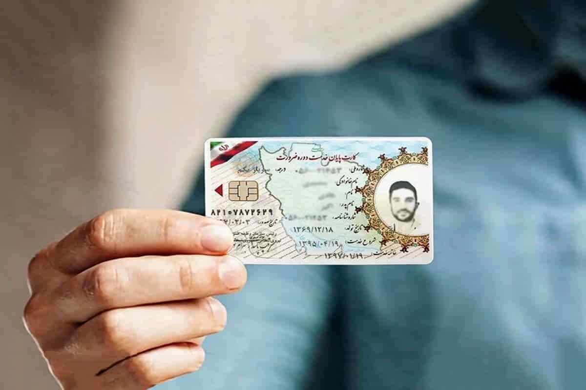 تصویر دست فردی که یک کارت پایان خدمت دوران سربازی را در دست دارد. کارت دارای یک تراشه در سمت چپ و یک عکس از دارنده کارت در سمت راست است. روی کارت متنی به خط فارسی و یک پرچم کوچک در گوشه بالا سمت چپ وجود دارد.